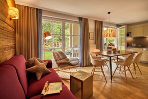 A modern living room with a red sofa, a wooden coffee table, and a dining area with a wooden table and chairs. - Appartamenti La Sajun e Les Viles (Badia)