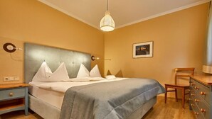 A bedroom with a bed, bedside table, dresser, chair, and a chandelier. - Appartamenti La Sajun e Les Viles (Badia)