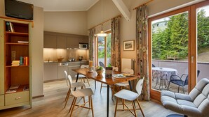 A modern kitchen with a dining area, wooden flooring, and a view of the outdoors. - Appartamenti La Sajun e Les Viles (Badia)