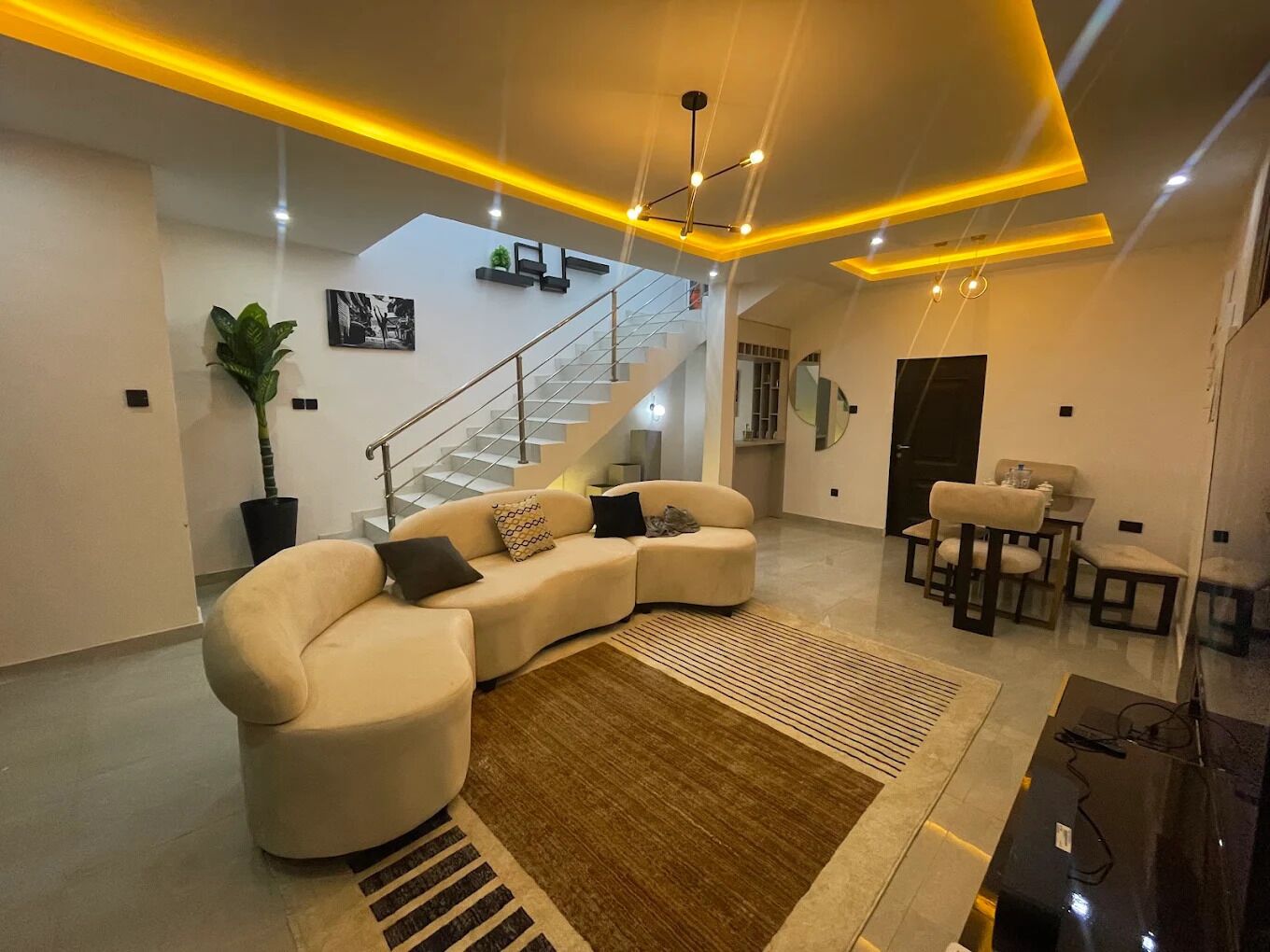 A modern living room with a sectional sofa, a staircase, and a dining area.