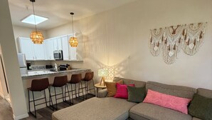 Ein modernes Wohnzimmer mit einer Eckcouch, einem runden Couchtisch und einer Küche im Hintergrund.