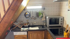 Eine kleine Küche mit Holzausstattung, einer Mikrowelle und einer hängenden Küchenutensilienstange.
