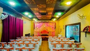Un salón con filas de sillas, un escenario con cortinas y luces en el techo.