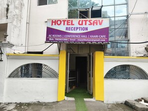 A hotel reception with a signboard indicating services like AC rooms, conference hall, and kaari cafe. - APS Hotel Utsav (Dehradun)