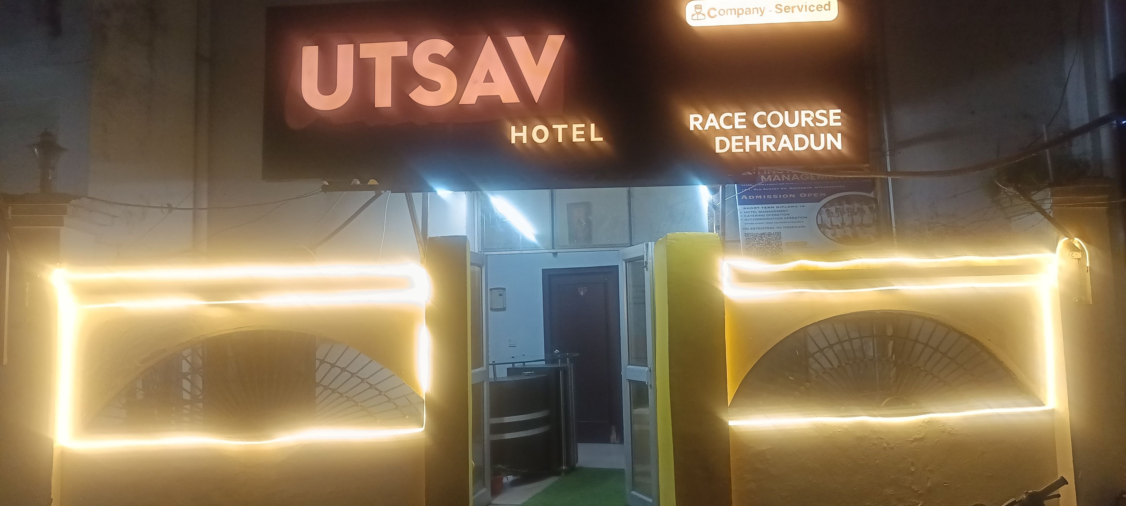 Entrada de un hotel con un cartel que dice UTSAV HOTEL y un hipódromo en Dehradun.