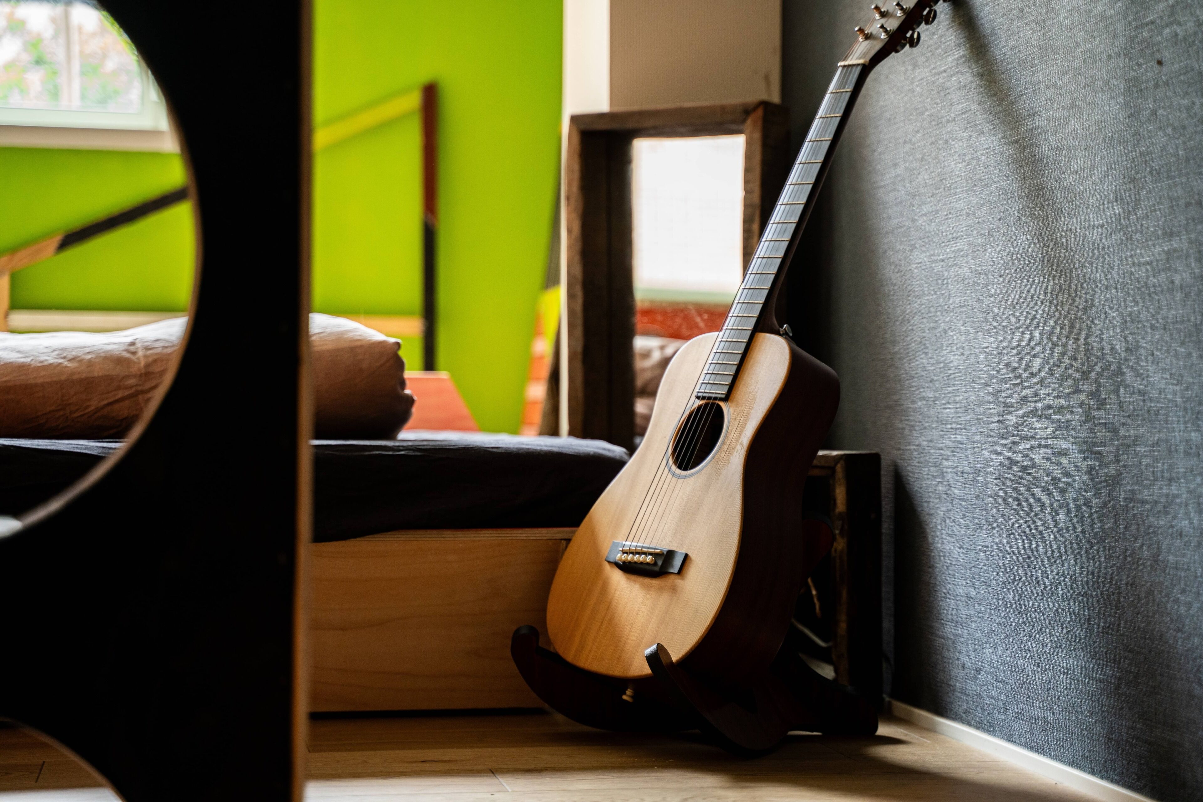 A guitar leaning against a wall in a room with a green wall and a window.