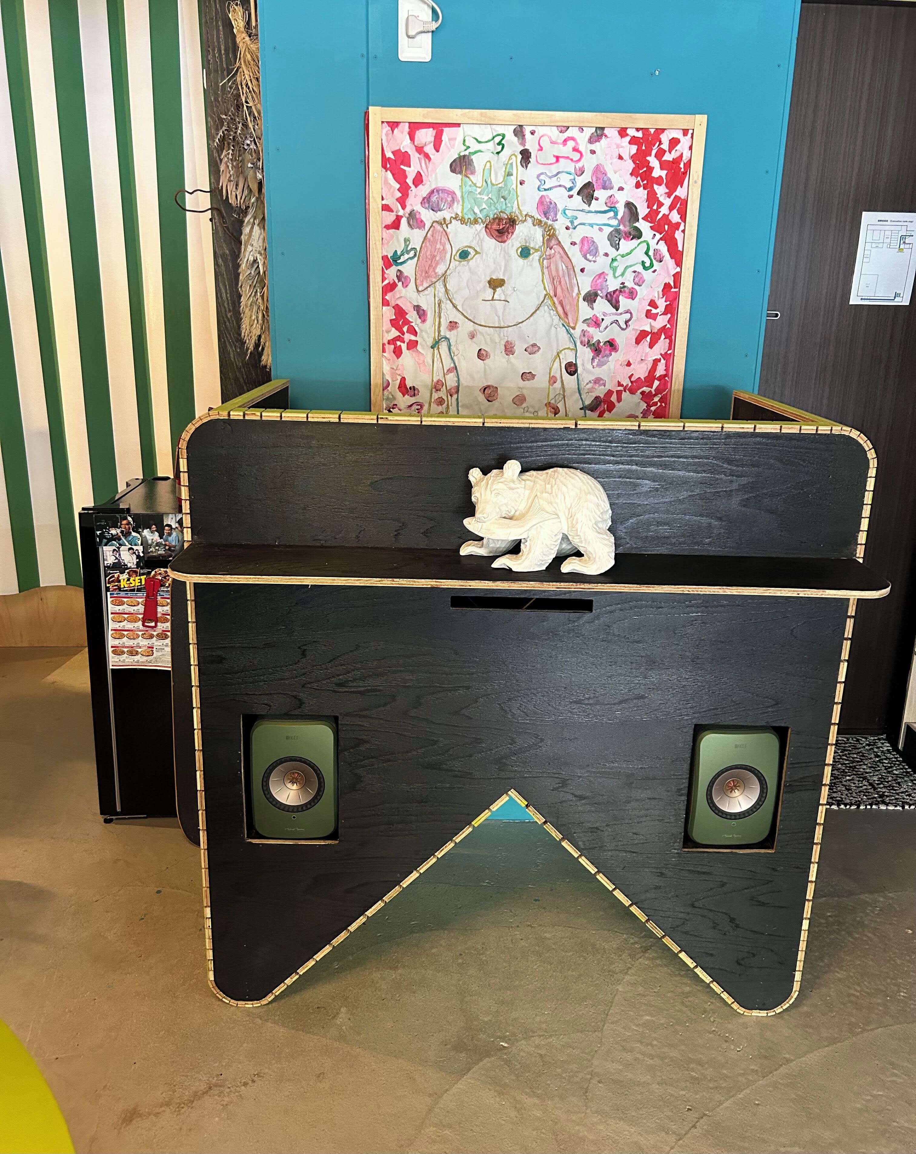 A room with a black chest-shaped table with a white animal figurine, a colorful painting on the wall, and a small black cabinet with a menu.