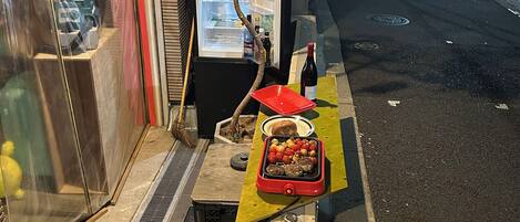 A street-side food stall with a display of food items and a bottle of wine.