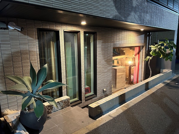 A modern building facade with a security camera, a potted plant, and a window with a view of a room inside. - Lab8 Tokyo (Tokyo)