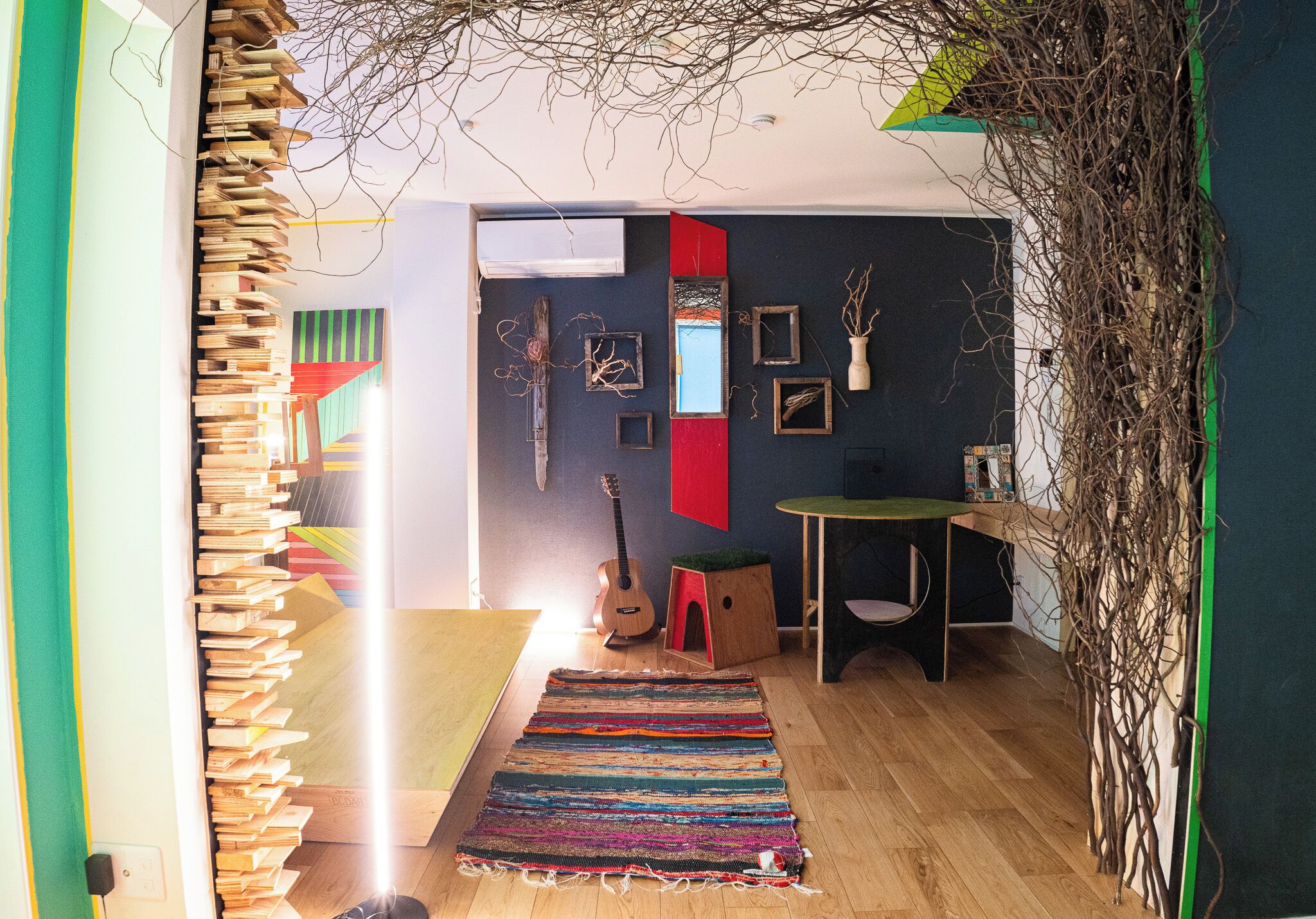 Une pièce avec une bibliothèque en bois, un tapis coloré, une guitare et une petite table dont le plateau est vert.