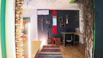 A room with a wooden bookshelf, a colorful rug, a guitar, and a small table with a green top.