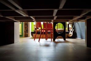 Una habitación con piso de madera, una mesa de comedor con sillas, una guitarra y una cama con pared verde al fondo.