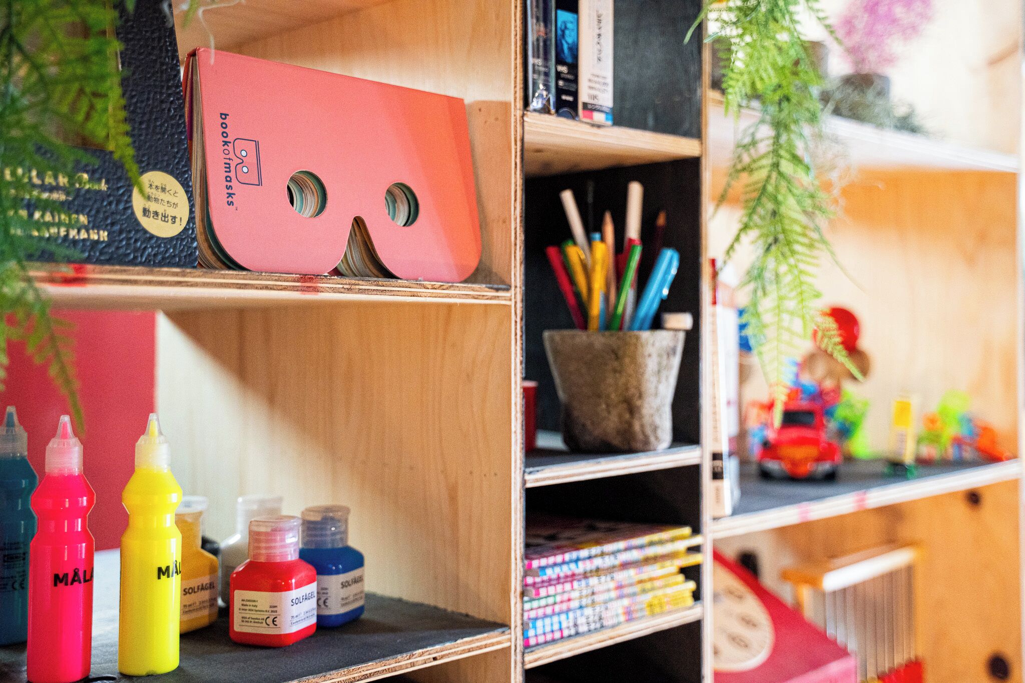 A shelf with various items including a red book, paint bottles, and a small toy car.