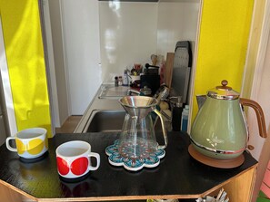 Una encimera de cocina con una cafetera, una jarra de café y dos tazas.