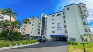 A multi-story hotel with a prominent 'Beach Palms' sign, a parking lot, and a clear sky. - Treat Yourself to Breathtaking Beachfront Views in this Sunlit and Spacious Corner Gem! (Indian Shores)