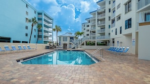 A swimming pool with lounge chairs, a staircase, and a building with balconies. - Treat Yourself to Breathtaking Beachfront Views in this Sunlit and Spacious Corner Gem! (Indian Shores)