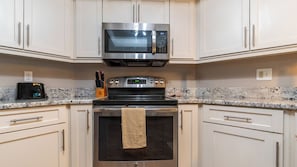 A kitchen with white cabinets, a stainless steel microwave, a black oven, and a granite countertop. - Treat Yourself to Breathtaking Beachfront Views in this Sunlit and Spacious Corner Gem! (Indian Shores)