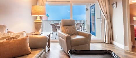 Una habitación con sofá, una silla, una lámpara, una bandeja y vistas al exterior.