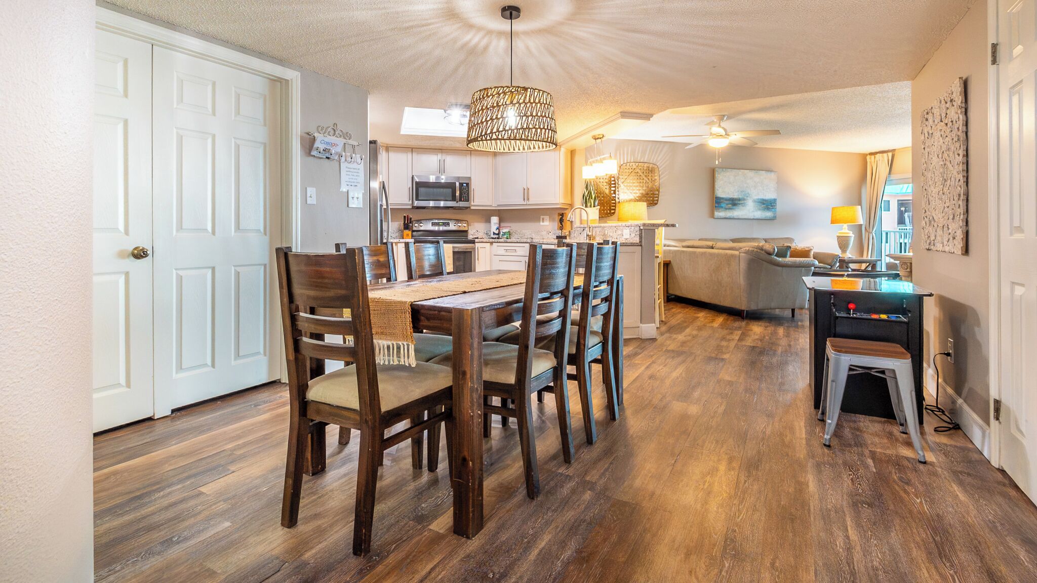 Une cuisine spacieuse dotée d’appareils électroménagers modernes, un coin repas avec des chaises en bois et un salon confortable avec un canapé et des lampes décoratives.
