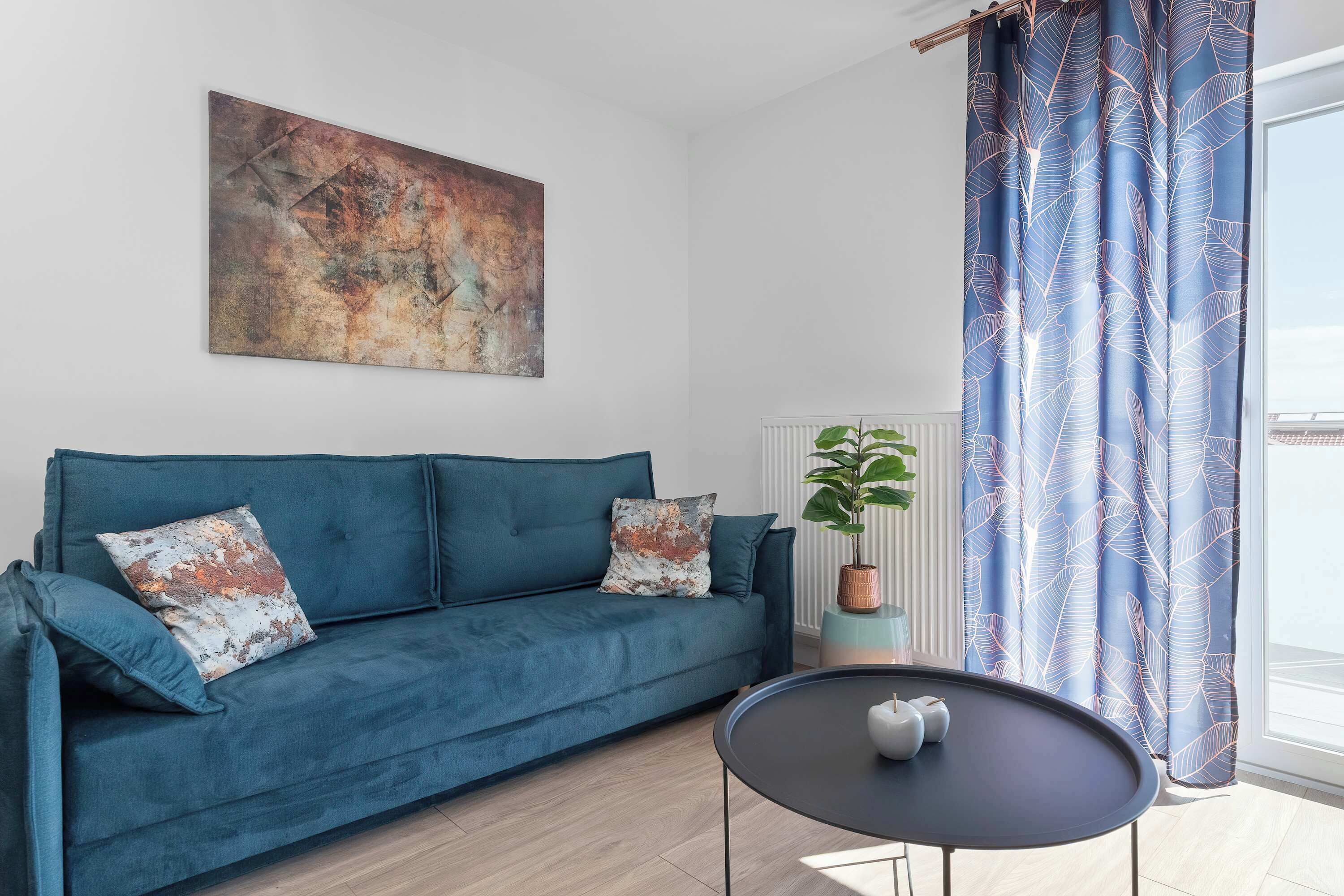 A living room with a blue sofa, a coffee table, a plant, and a large abstract painting on the wall.