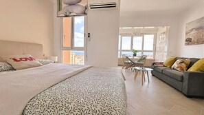 Ein Schlafzimmer mit Bett, Sofa, Esstisch und Stühlen sowie einem großen Fenster.