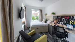Ein modernes Hotelzimmer mit Bett, Schreibtisch, Stuhl und Fernseher an der Wand.