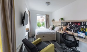A modern hotel room with a bed, desk, chair, and a television on the wall. - Student Only The Arch (Liverpool)