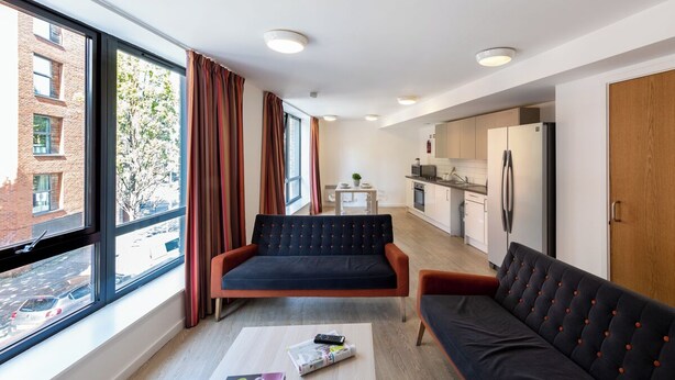 Ein modernes Apartment mit einer Couch, einem kleinen Tisch mit Fernbedienung und einer Küchenzeile.