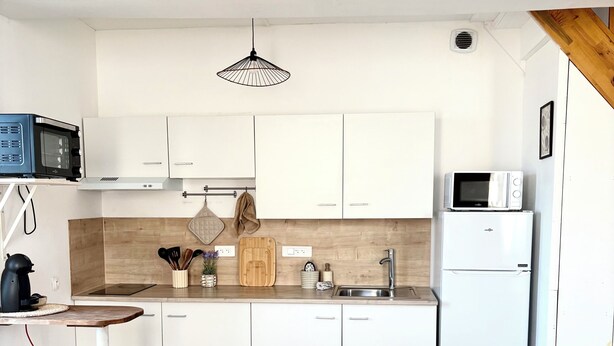 Una cocina moderna con armarios blancos, una mesa de comedor de madera para cuatro personas y un microondas en la encimera.