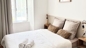 Una cama bien hecha con toallas enrolladas, una lámpara de noche y un cuadro en la pared.