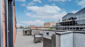A rooftop terrace with wicker furniture and a modern building in the background. - Lovely Beachside 2-Bedroom Apartment (Santa Monica)
