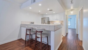 A modern kitchen with a central island, bar stools, and a view into the living area. - Lovely Beachside 2-Bedroom Apartment (Santa Monica)