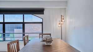 A dining table with chairs, a decorative centerpiece, a window with a view of a brick building, and a wall-mounted light fixture. - Lovely Beachside 2-Bedroom Apartment (Santa Monica)