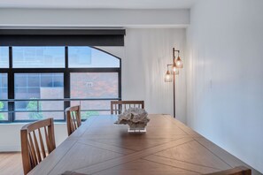 A dining table with chairs, a decorative centerpiece, a window with a view of a brick building, and a wall-mounted light fixture. - Lovely Beachside 2-Bedroom Apartment (Santa Monica)