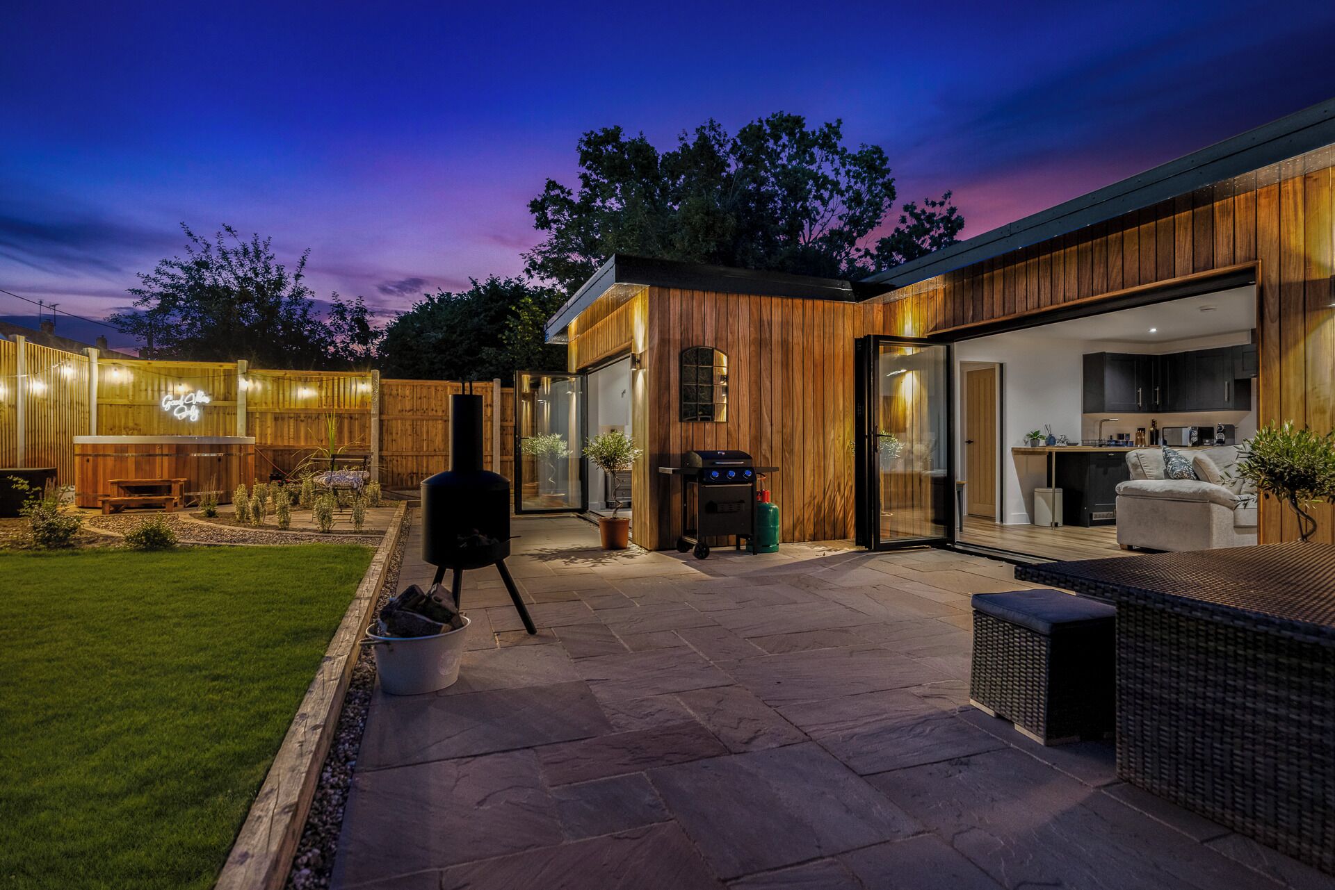 A modern house with a patio, a barbecue, and a kitchen visible through glass doors.