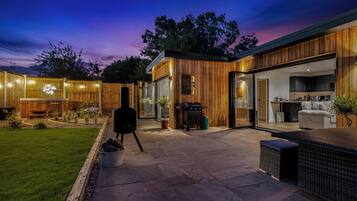 A modern house with a patio, a barbecue, and a kitchen visible through glass doors.