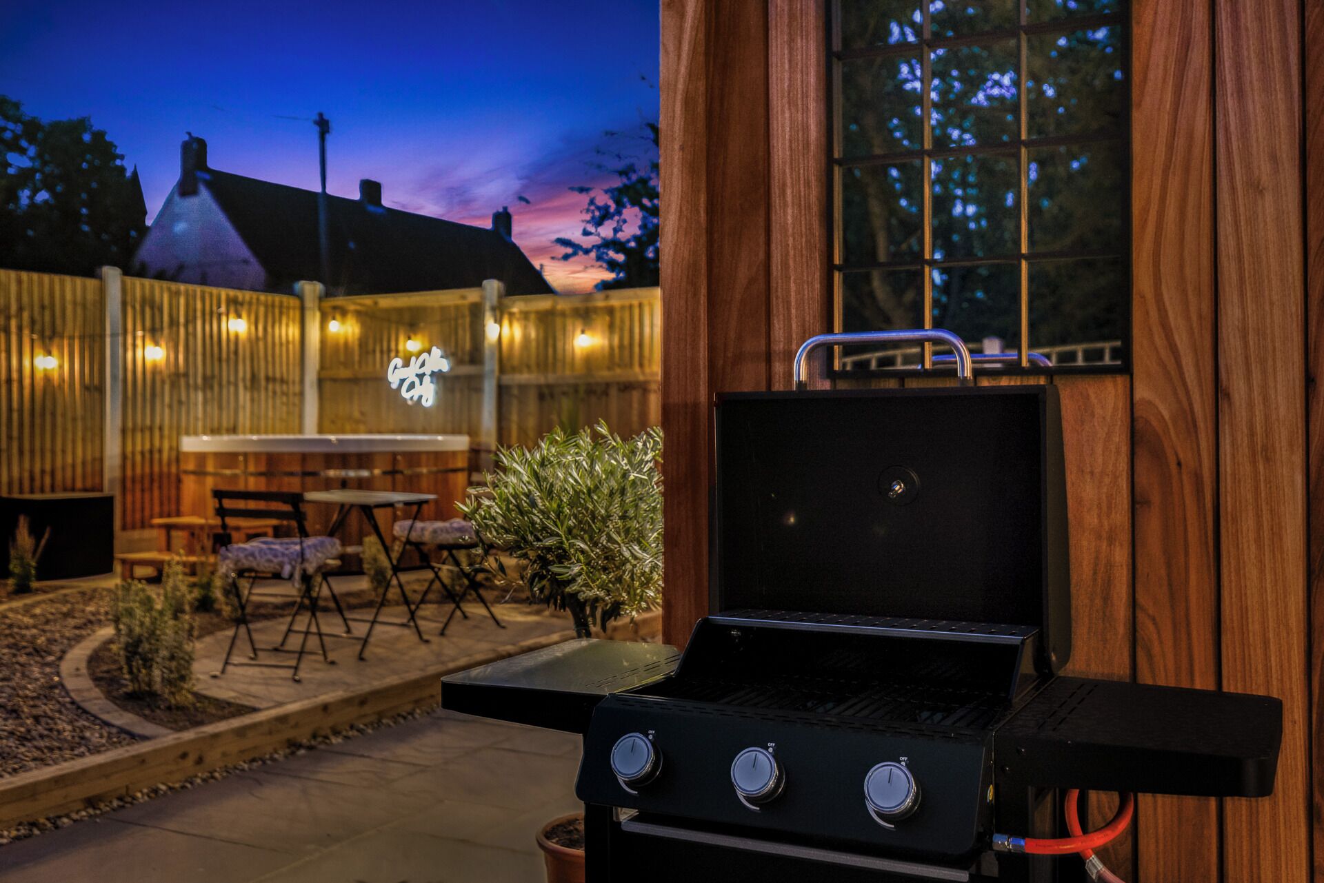 En udendørs patio med grill, træterrasse og et bord med stole.