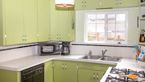 Une cuisine avec des meubles de rangement verts, un four à micro-ondes, une machine à café, un évier et une cuisinière.