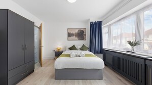 Une chambre moderne avec un grand lit, une armoire, une table de chevet et une fenêtre avec des rideaux.