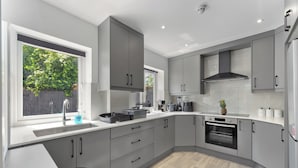 Une cuisine moderne avec des meubles gris, un four encastré et une fenêtre donnant sur un paysage verdoyant.