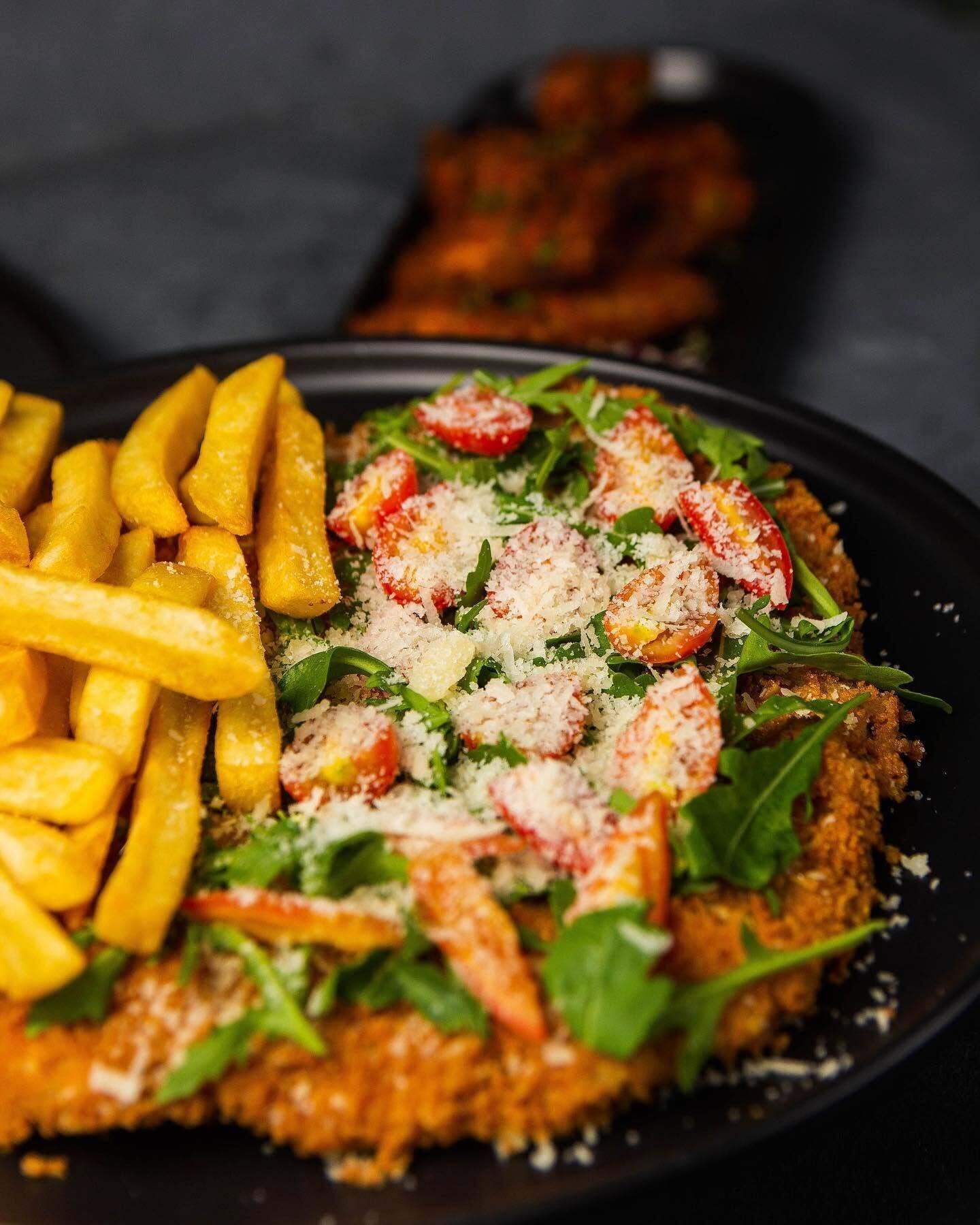 A plate with a breaded and fried item, possibly chicken, topped with cherry tomatoes, cheese, and greens, accompanied by French fries.