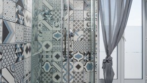 Une douche avec des carreaux décorés, une porte en verre et un rideau.