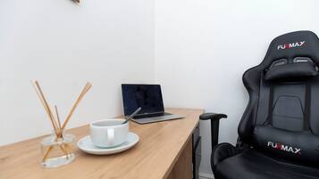 A room with a wooden desk, a laptop, a white cup with a saucer, a black gaming chair labeled 'FURMAX,' and a picture frame on the wall.