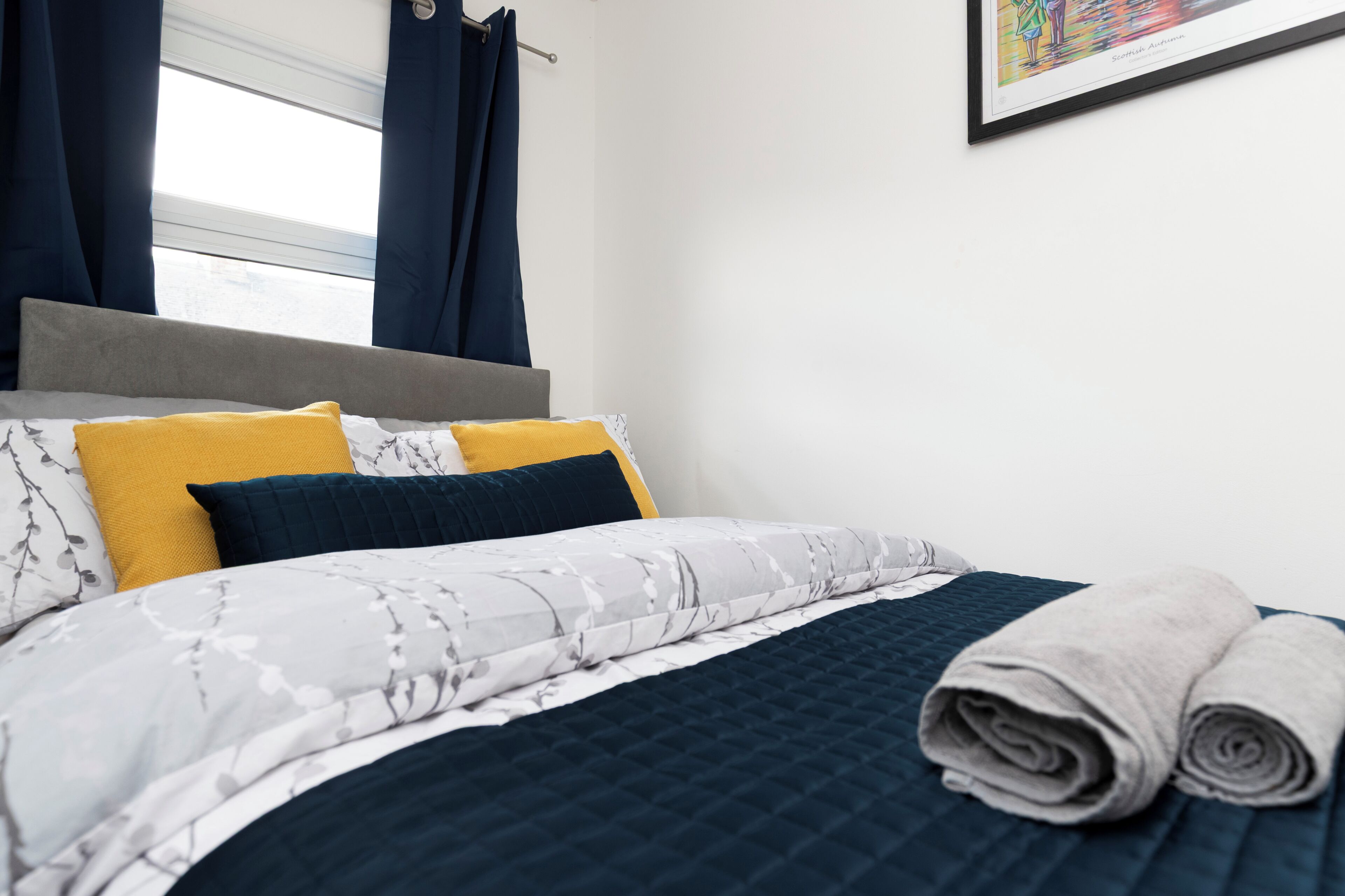 A neatly made bed with a patterned bedspread, two pillows, and rolled towels.