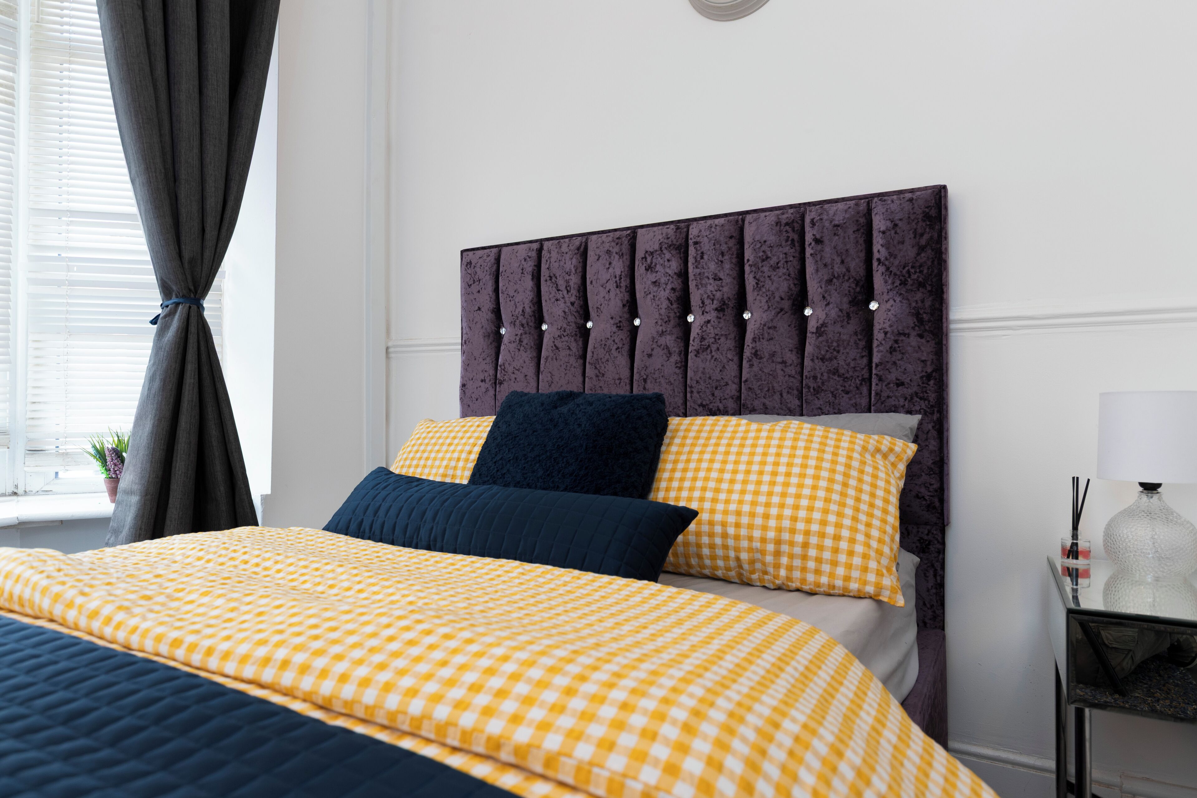 A neatly made bed with a checkered bedspread, a tufted headboard, and two pillows.