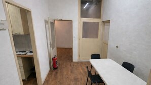 A room with a long table, chairs, a fire extinguisher, and a door leading to another room.