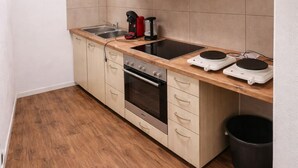 A compact kitchen with a built-in oven, a coffee maker, and a black trash bin.