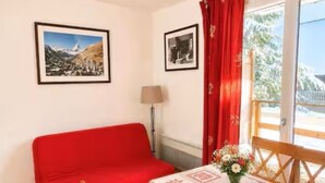 A room with a red sofa, a table with a floral tablecloth, and two framed pictures on the wall. - A Nature Getaway in the Mountains: A Quiet Apartment (Besse-et-Saint-Anastaise)