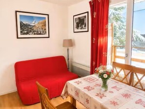 Una habitación con un sofá rojo, una mesa con mantel floreado y dos cuadros en la pared.