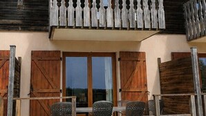 A wooden building with a balcony, wooden shutters, and a table with chairs. - A Nature Getaway in the Mountains: A Quiet Apartment (Besse-et-Saint-Anastaise)